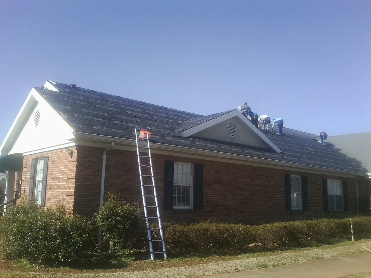 Crew tearing shingles off a brick ranch roof with a ladder set — Emergency Roof Repair work by our crew in Tracy