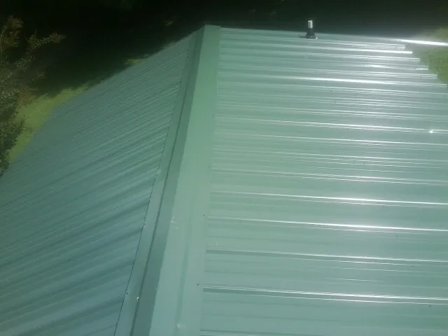 New green metal panels meeting at the ridge of a roof — Flat Roof Repair work by our crew in Tracy
